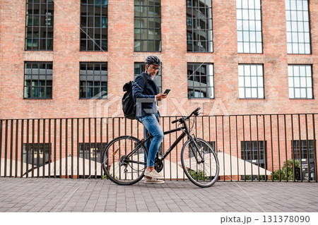 City commuter riding bike from work, reading text message on phone. 131378090