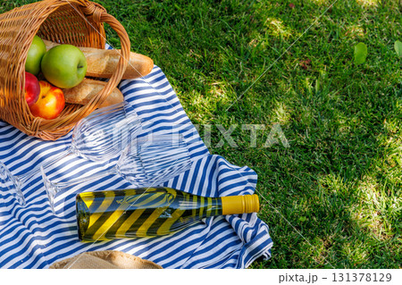 Picnic basket with wine, fruits, and baguette on a sunny green meadow 131378129