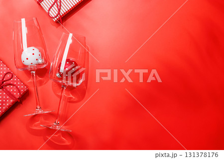 Wine glasses with Christmas baubles inside on red background, mockup for holiday card or invitation 131378176