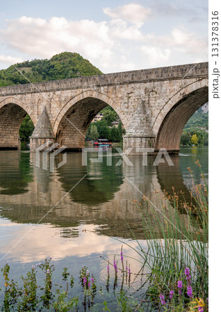 An ancient stone bridge with arches spanning the tranquil Drina River with wild flowers An ancient stone bridge with arches spanning the tranquil Drina River with wild flowers 131378316