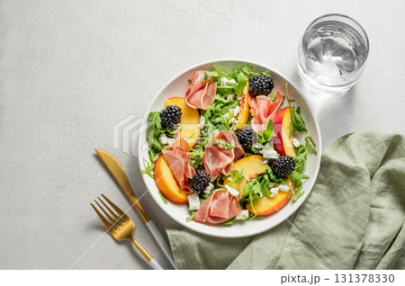 Fresh salad with peaches, arugula, feta, prosciutto and berries in a plate on a light background 131378330