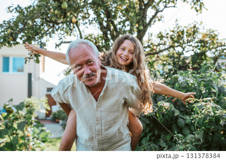 Grandfather playing with granddaughter in the garden. 131378384