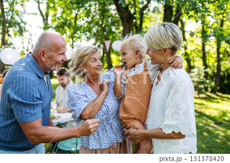 Smiling senior couple with grandchild and daughter at family gathering. 131378420