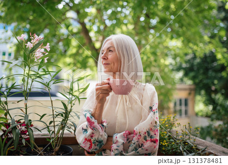 Portrait of beautiful senior woman standing on balcony with morning cup of coffee. Portrait of beautiful senior woman standing on balcony with morning cup of coffee. 131378481
