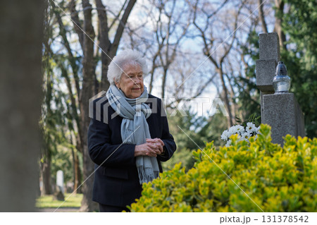 Elderly woman praying at a grave. Elderly woman praying at a grave. 131378542