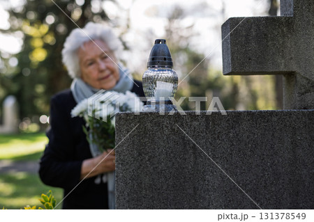 Old woman lighting a candle at a grave. Old woman lighting a candle at a grave. 131378549