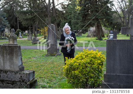 Elderly woman visiting a grave on All Saints Day. Elderly woman visiting a grave on All Saints Day. 131378558