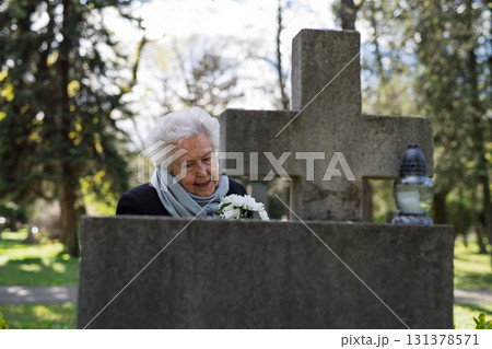 Senior woman crying and mourning at a grave on cemetery. 131378571