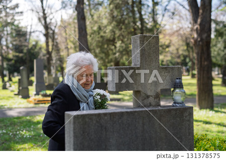 Elderly woman visiting a grave on All Saints Day. Elderly woman visiting a grave on All Saints Day. 131378575