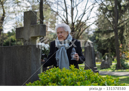 Old woman lighting a candle at a grave. 131378580
