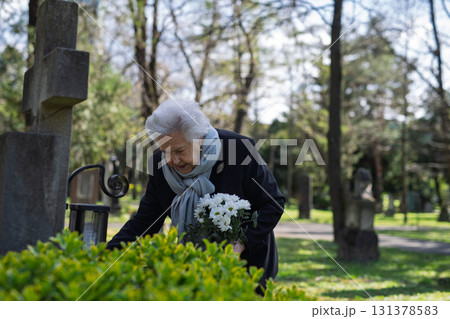 Elderly widow bringing flowers to a grave at cemetery. Elderly widow bringing flowers to a grave at cemetery. 131378583