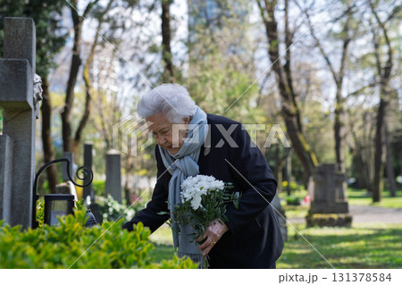 Elderly widow bringing flowers to a grave at cemetery. Elderly widow bringing flowers to a grave at cemetery. 131378584