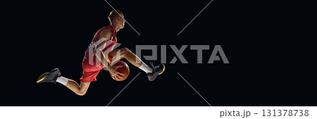 Basketball player in mid-air holding ball with determination on dark background 131378738