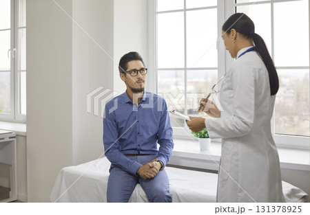 Handsome guy with glasses at doctor's appointment listens attentively to the doctor in modern office of medical institution. 131378925