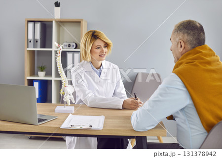 Young woman doctor with medical spine model on desk talking to senior man patient Young woman doctor with medical spine model on desk talking to senior man patient 131378942
