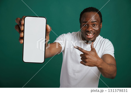Smartphone with white empty space for text. African American man is standing against green background in the studio 131379831