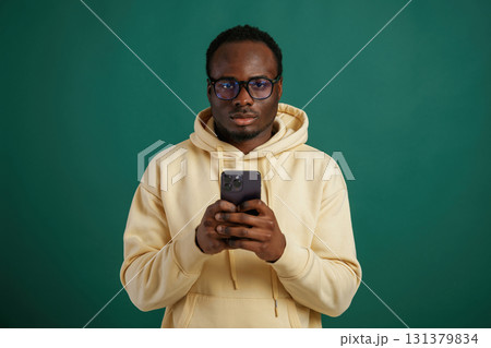 Using smartphone. African American man is standing against green background in the studio 131379834
