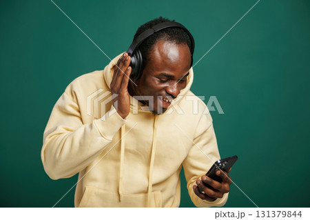 In headphones, enjoying music. African American man is standing against green background in the studio In headphones, enjoying music. African American man is standing against green background in the studio 131379844