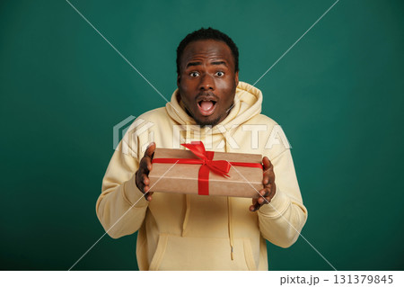 In shock. Holding gift box. African American man is standing against green background in the studio 131379845