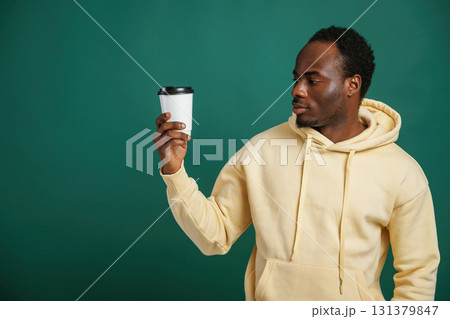Coffee cup in hand. African American man is standing against green background in the studio Coffee cup in hand. African American man is standing against green background in the studio 131379847