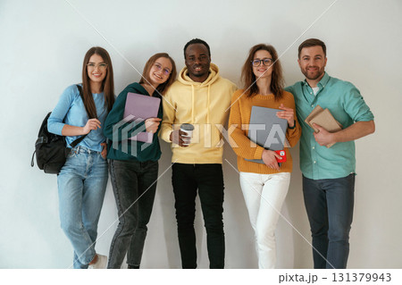 Holding notepads and coffee cup. Group of young people are standing against white background Holding notepads and coffee cup. Group of young people are standing against white background 131379943