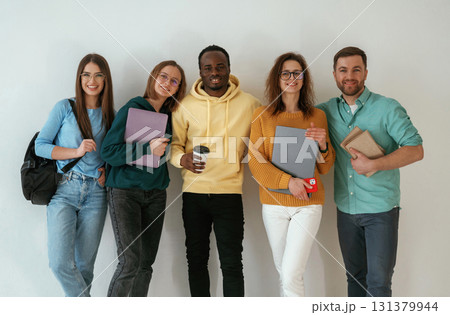 Holding notepads and coffee cup. Group of young people are standing against white background Holding notepads and coffee cup. Group of young people are standing against white background 131379944