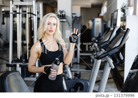 Athletic woman showing ok sign while holding water bottle in gym Athletic woman showing ok sign while holding water bottle in gym 131379996