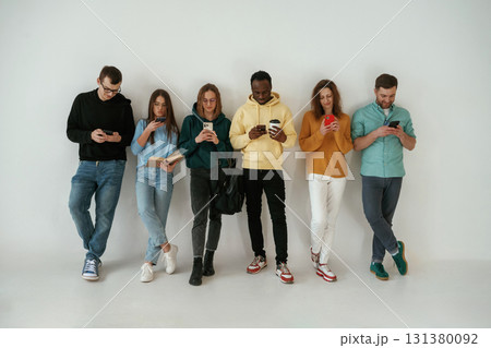 With smartphones in hands. Group of young people are standing against white background With smartphones in hands. Group of young people are standing against white background 131380092