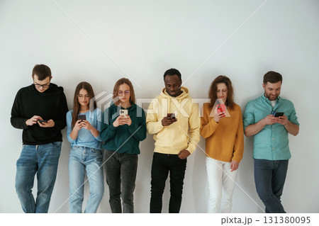 Busy by using smartphones. Group of young people are standing against white background 131380095