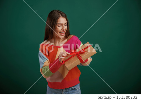 Holidays time. Holding gift box. Young woman is standing against green background in the studio 131380232