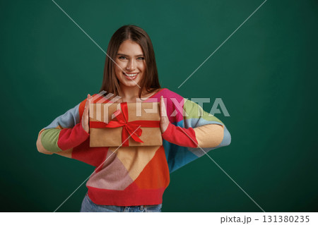 Holidays time. Holding gift box. Young woman is standing against green background in the studio Holidays time. Holding gift box. Young woman is standing against green background in the studio 131380235