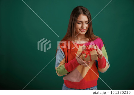 Little present in hands. Gift box. Young woman is standing against green background in the studio 131380239