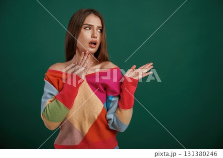 Thoughtful facial expression. Young woman is standing against green background in the studio 131380246