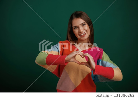 Heart shaped gesture by hands, sending love. Young woman is standing against green background in the studio Heart shaped gesture by hands, sending love. Young woman is standing against green background in the studio 131380262