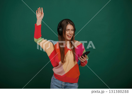 Feel the rhythm, listening to the music. Young woman is standing against green background in the studio Feel the rhythm, listening to the music. Young woman is standing against green background in the studio 131380288