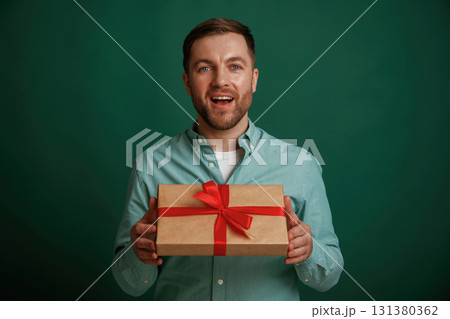 Little gift box in hands. Man is standing against background in the studio Little gift box in hands. Man is standing against background in the studio 131380362