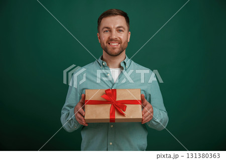 Little gift box in hands. Man is standing against background in the studio 131380363
