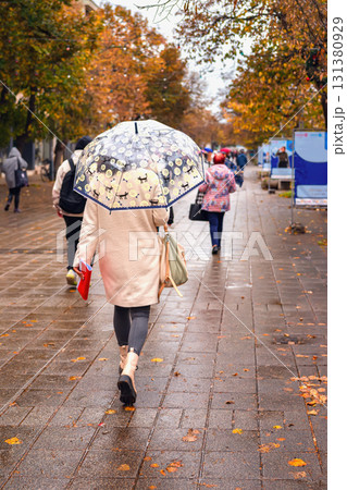 Woman walking down rainy autumn street with transparent umbrella. Concept of rainy day, street lifestyle, autumn, umbrella mood, rainy weather Woman walking down rainy autumn street with transparent umbrella. Concept of rainy day, street lifestyle, autumn, umbrella mood, rainy weather 131380929