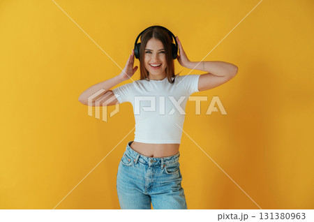 In headphones, enjoying music. Young woman is against yellow background In headphones, enjoying music. Young woman is against yellow background 131380963