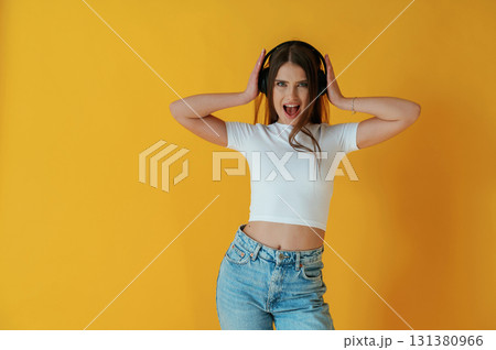 In headphones, enjoying music. Young woman is against yellow background 131380966