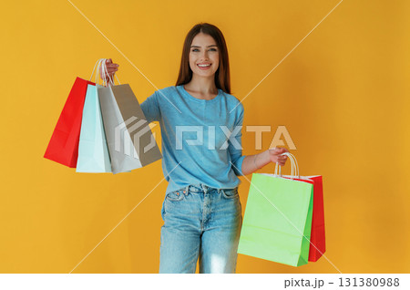 Shopping day, holding bags. Young woman is against yellow background Shopping day, holding bags. Young woman is against yellow background 131380988