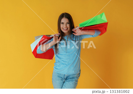 Standing and holding shopping bags. Young woman is against yellow background 131381002