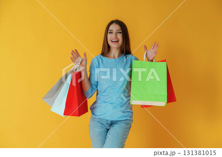 Smiling, happy, holding shopping bags. Young woman is against yellow background Smiling, happy, holding shopping bags. Young woman is against yellow background 131381015
