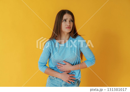 Having stomach pain. Young woman is against yellow background Having stomach pain. Young woman is against yellow background 131381017