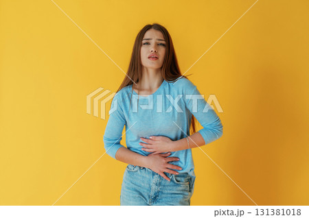 Having stomach pain. Young woman is against yellow background Having stomach pain. Young woman is against yellow background 131381018