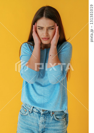 Bad headache. Young woman is against yellow background 131381019