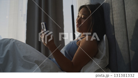 Beautiful Young Women Sitting in Bed and Scrolls Through News Feed on Smartphone 131381332