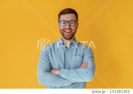 Standing with arms crossed. Attractive man in blue shirt is against yellow background 131381363