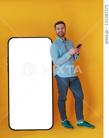 Big smartphone, place for copy space. Attractive man in blue shirt is against yellow background 131381375