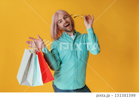 With shopping bags. Guy with pink hair is posing against yellow background With shopping bags. Guy with pink hair is posing against yellow background 131381399